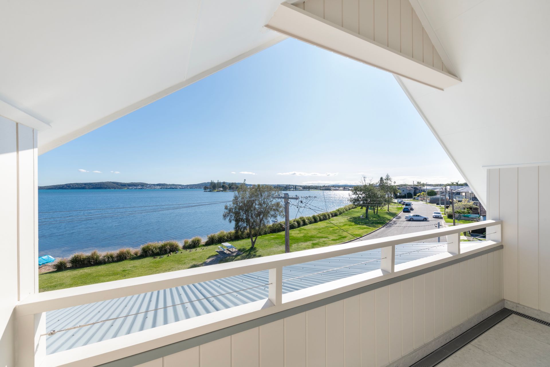 Balcony with white railing overlooking a blue bay and coastline on a sunny day — Indie Living In Bennetts Green, NSW