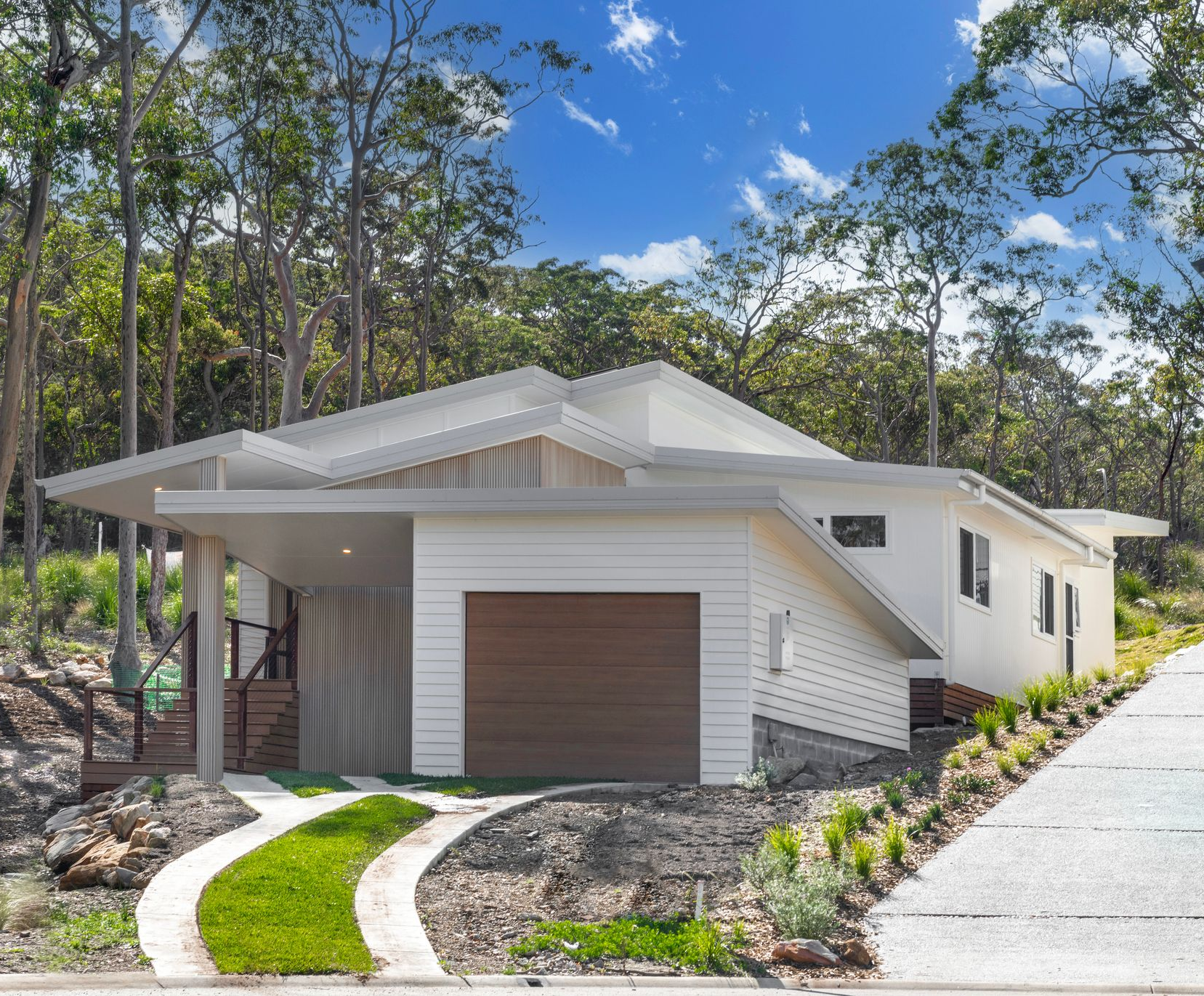 White modern house with carport and garage, driveway, surrounded by trees under a blue sky — Indie Living In Bennetts Green, NSW