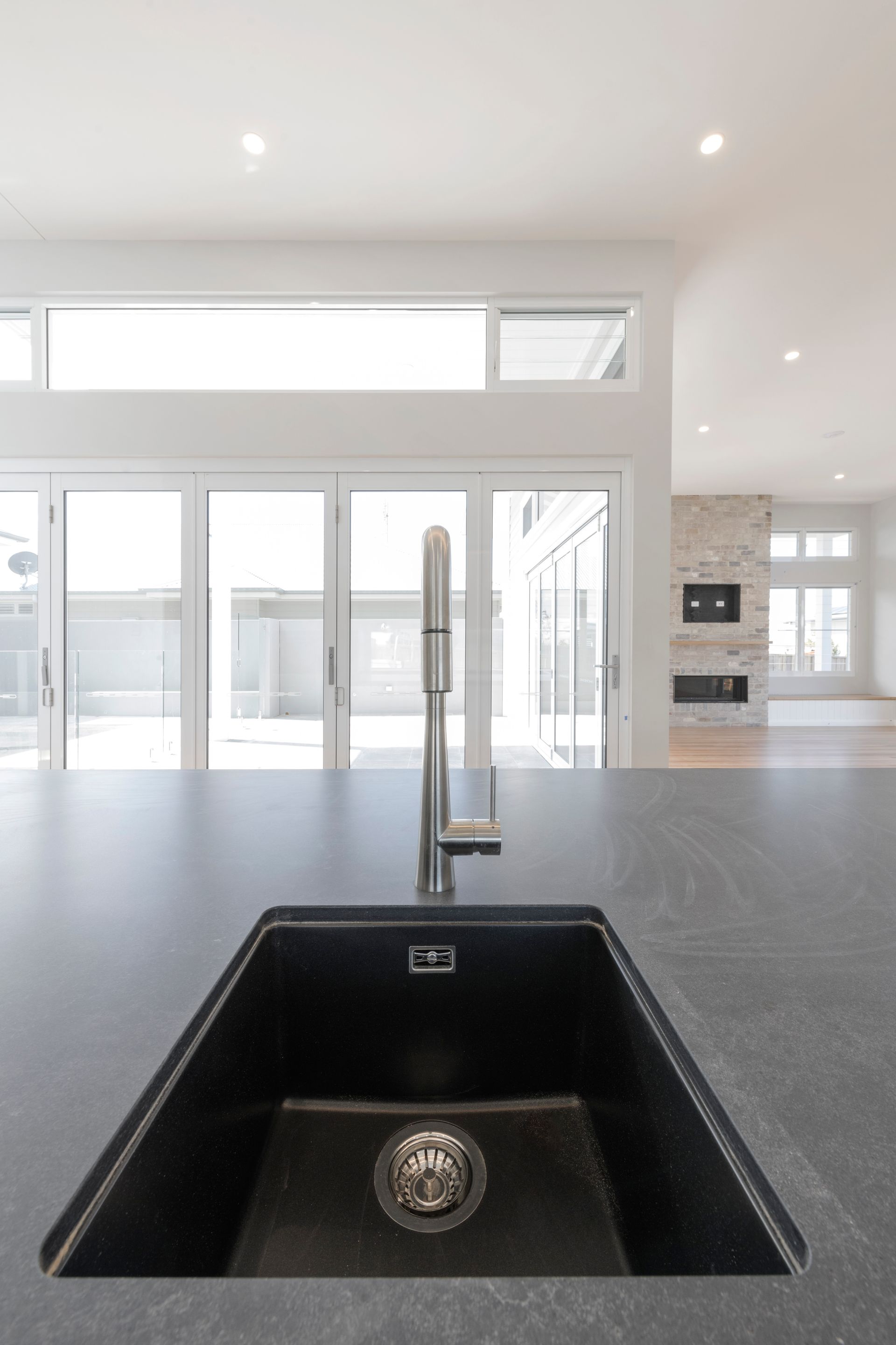 Black kitchen sink with chrome faucet on dark countertop, bright windows and open floor plan in the background — Indie Living In Lake Macquarie, NSW