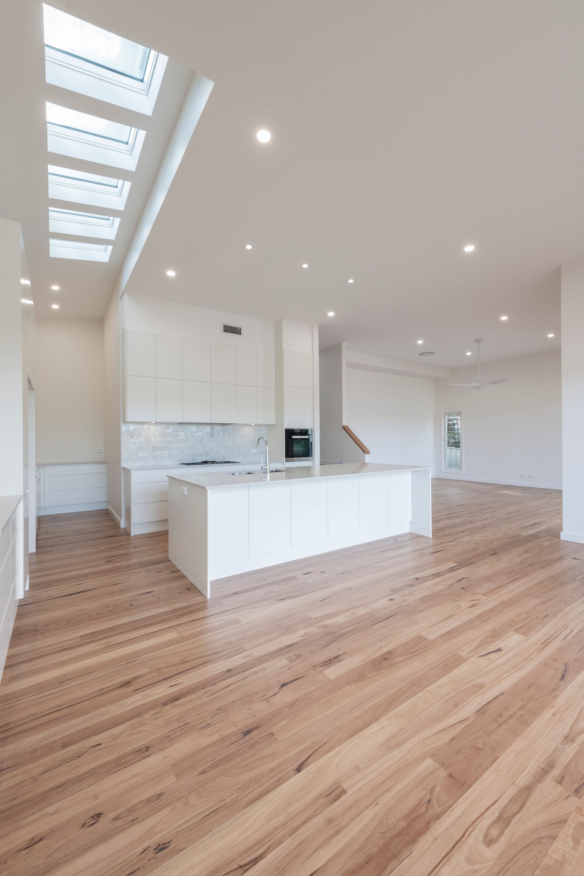 Spacious, modern kitchen with white cabinets, island bench, and wooden floors. Skylights illuminate the space — Indie Living In Hunter Valley, NSW