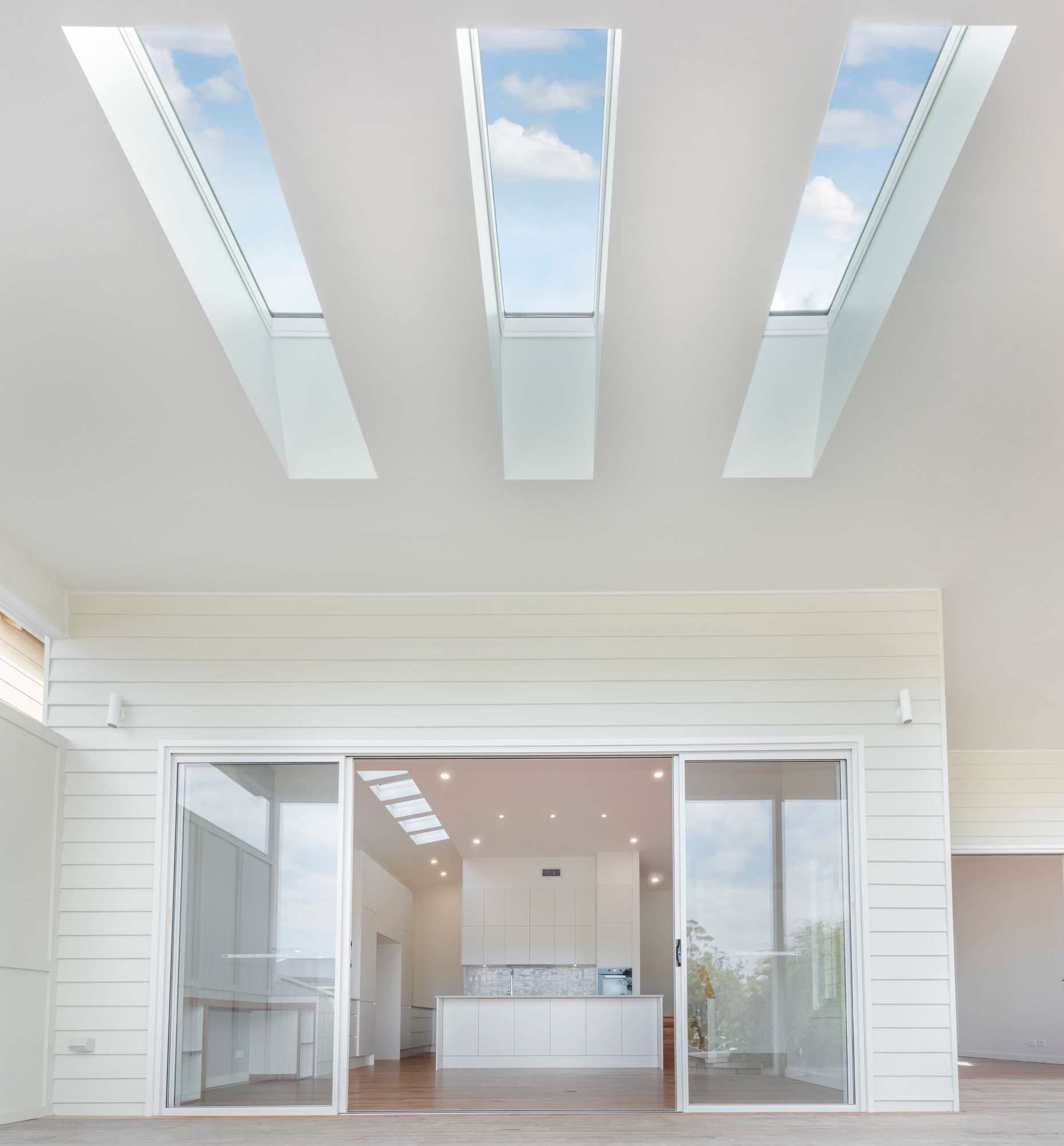 Bright interior with three long skylights. Sliding doors open to a white kitchen — Indie Living In Bennetts Green, NSW