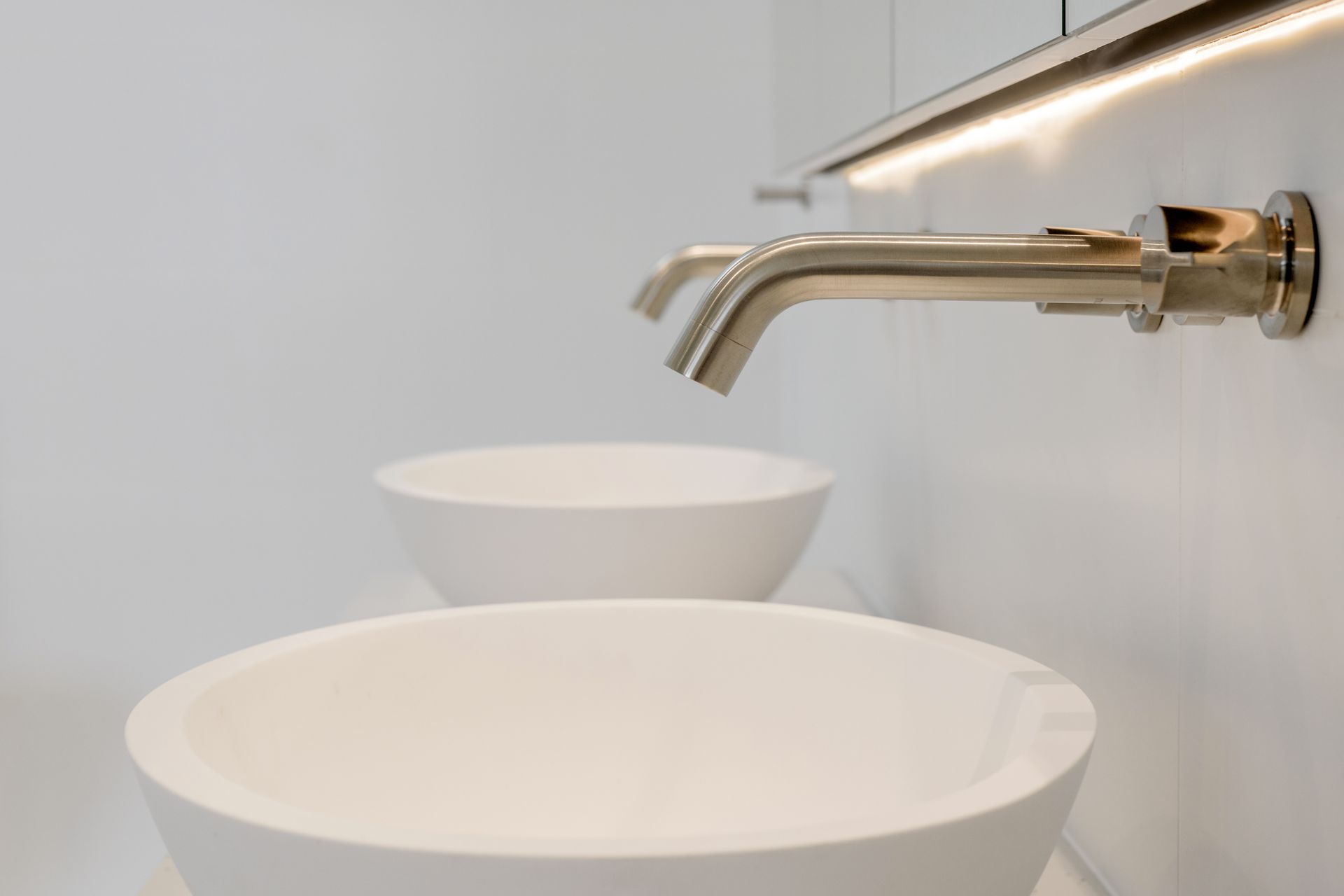 White sinks and silver faucets on a white wall with under-mirror lighting — Indie Living In Lake Macquarie, NSW