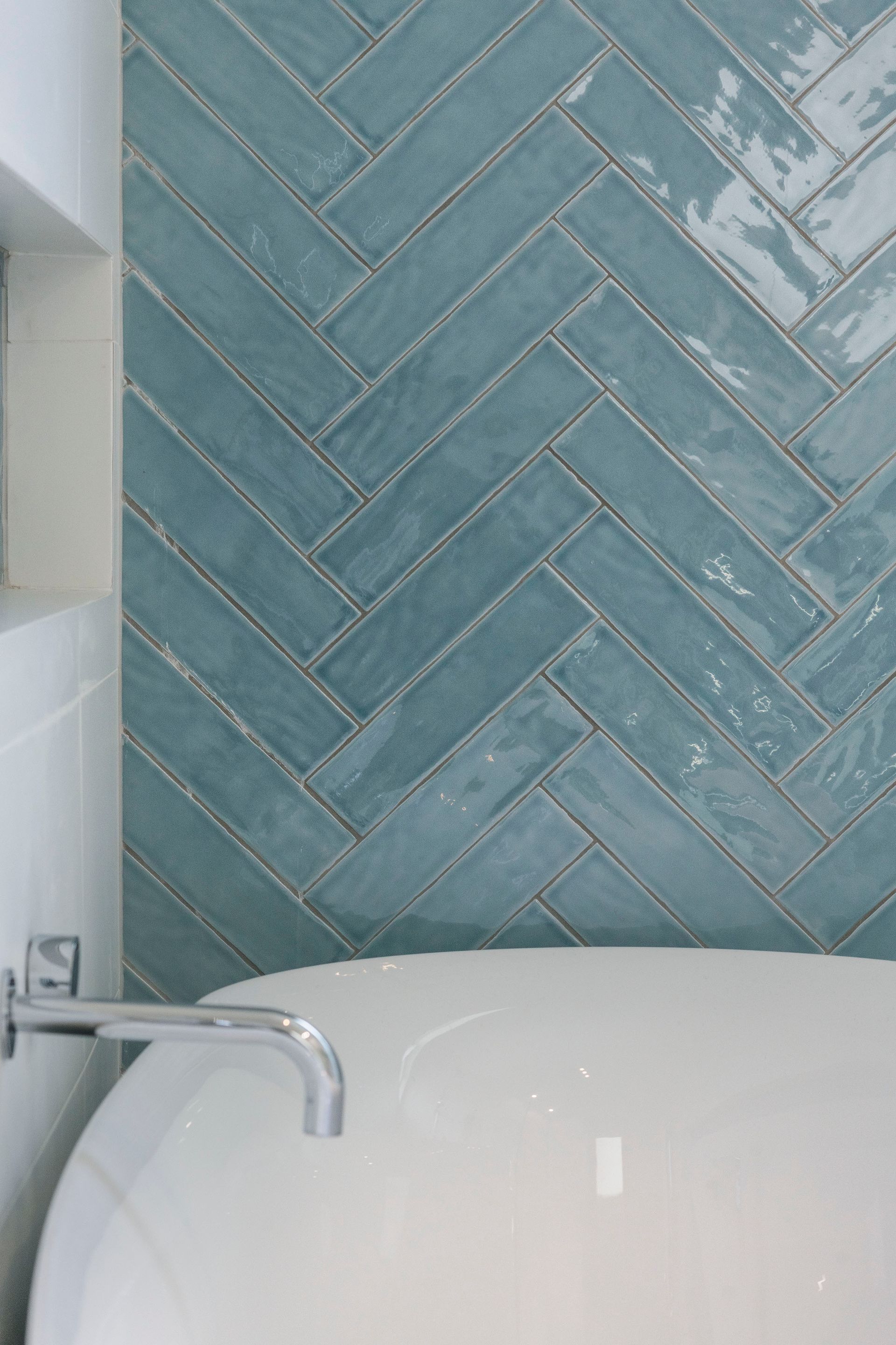 Blue herringbone tile wall above a white bathtub with chrome faucet — Indie Living In Lake Macquarie, NSW