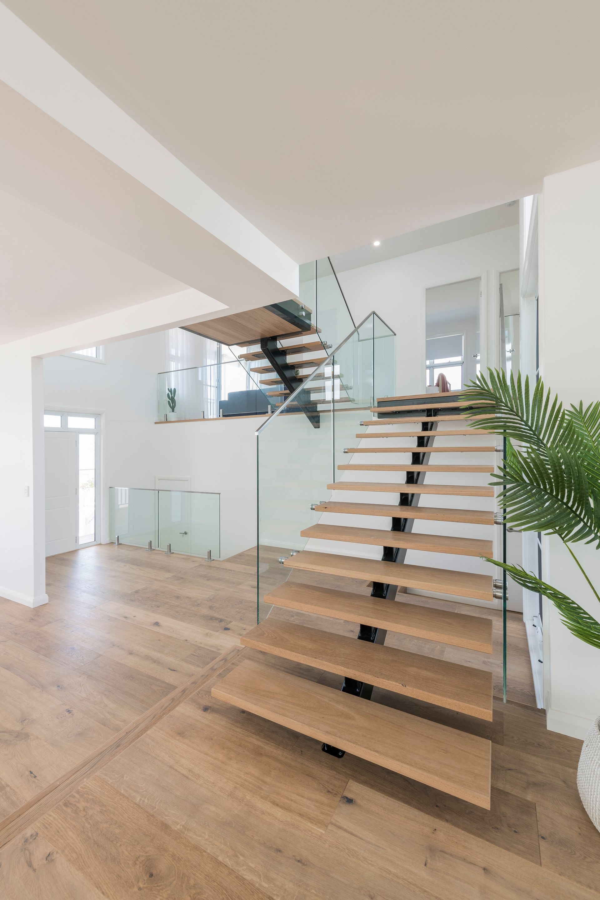 Modern interior with a wooden staircase, glass railing, and natural light — Indie Living In Bennetts Green, NSW