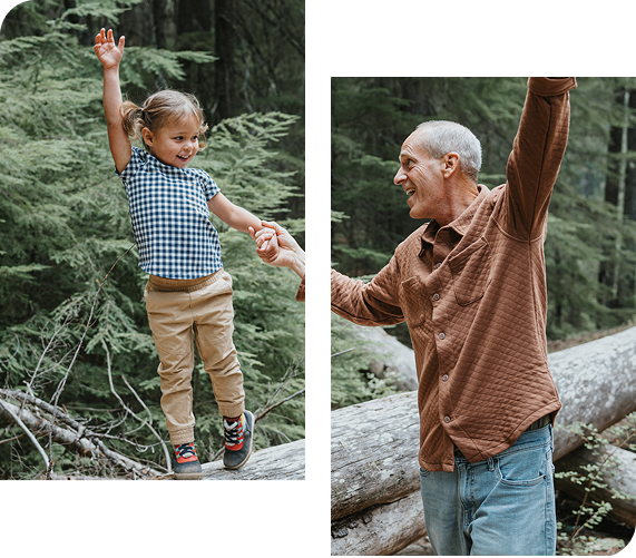 Girl and man balancing on a log in a forest, holding hands, arms raised in the air.