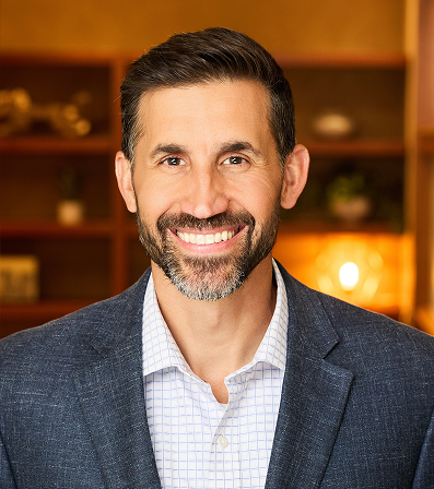 Man in glasses and blue suit smiles in an office setting.