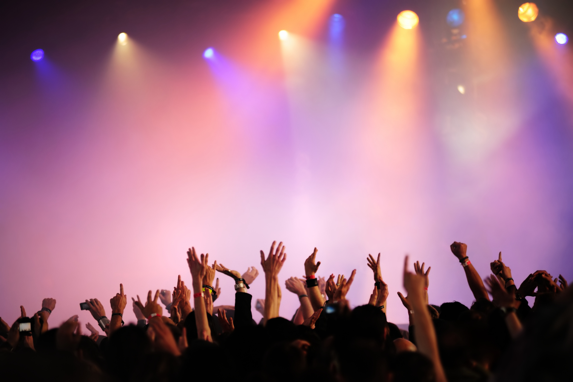 Concert crowd with raised hands silhouetted against stage lights and smoke