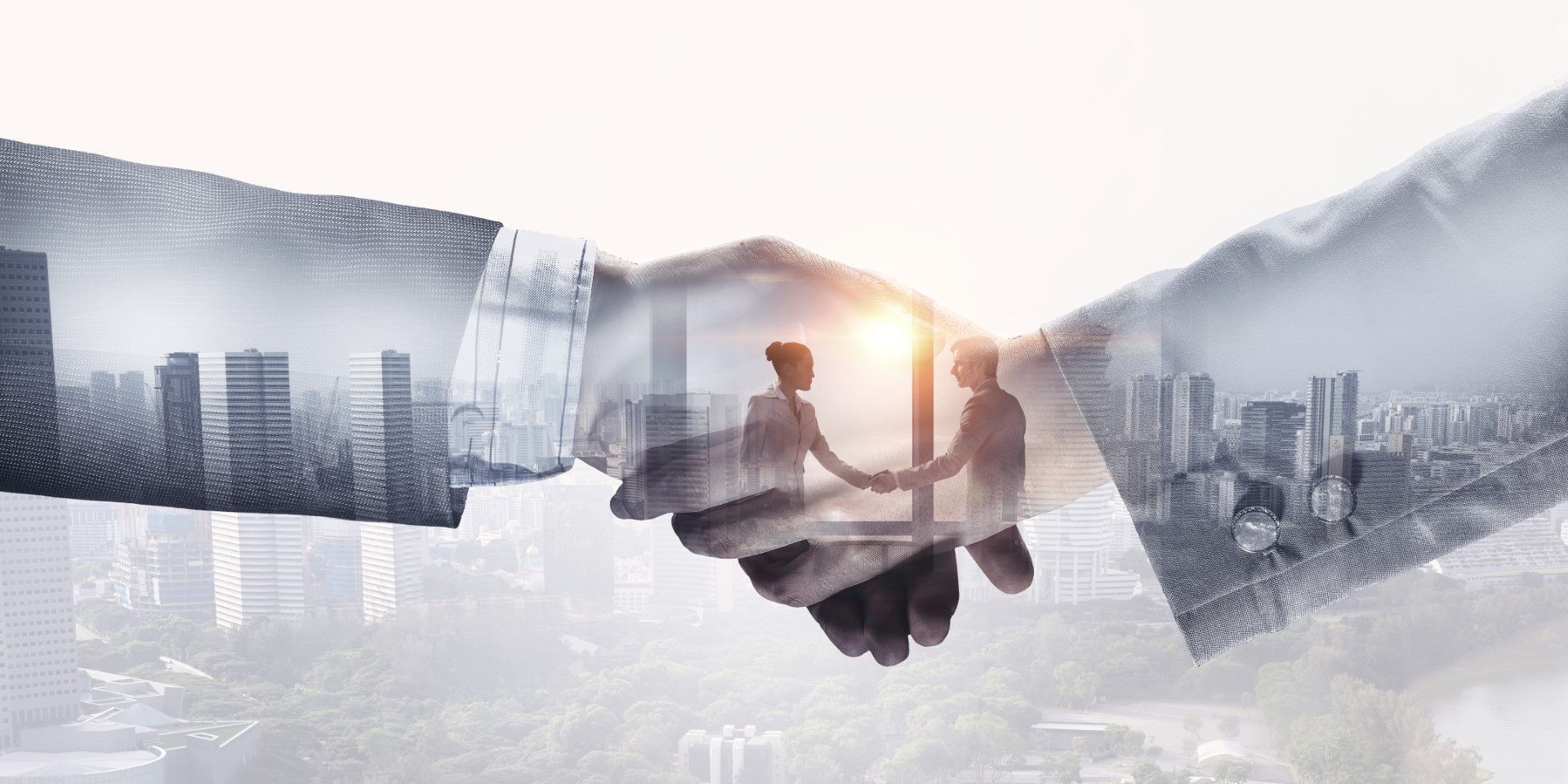 A double exposure of two people shaking hands with a city skyline in the background.
