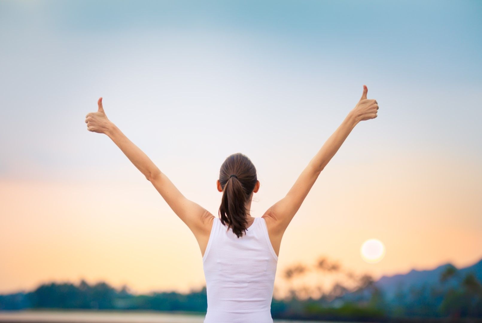 A woman is standing with her arms outstretched and giving a thumbs up.