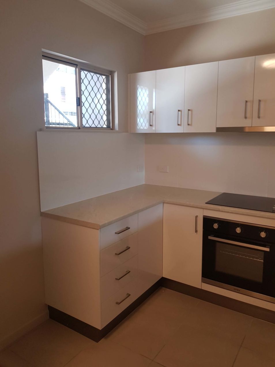 An Empty Kitchen With White Cabinets and a Window — Omni Builders In Bungalow, QLD