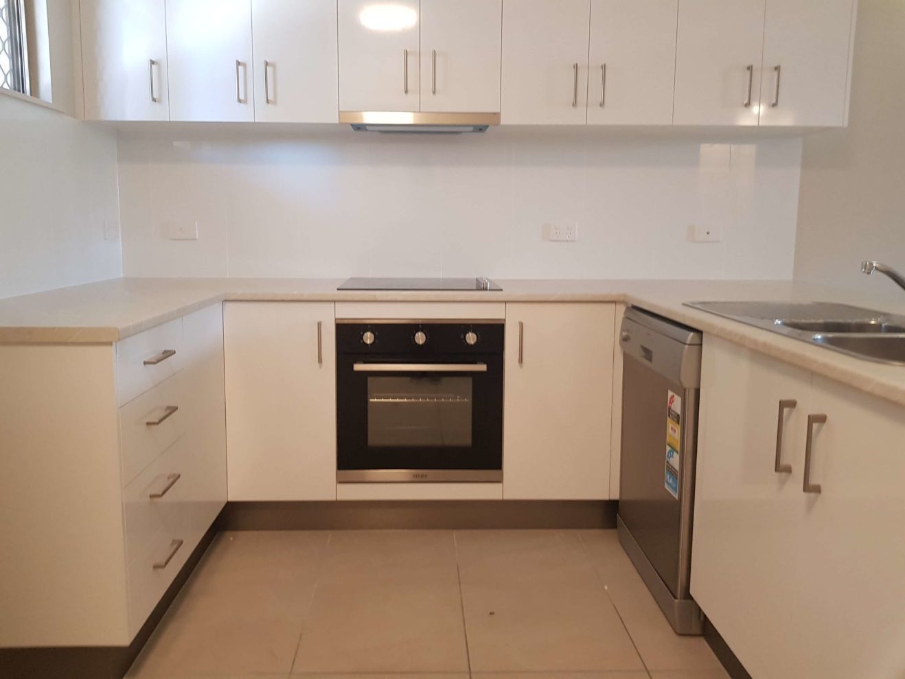 An Empty Kitchen With White Cabinets and a Black Oven — Omni Builders In Bungalow, QLD