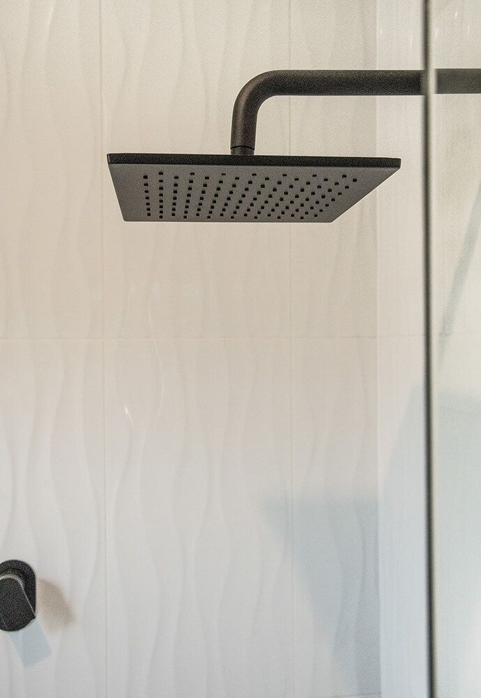 A Black Shower Head is Hanging From a Shower Head in a Bathroom — Omni Builders In Bungalow, QLD