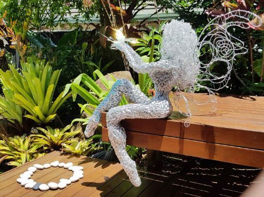 A Wire Sculpture of a Fairy is Sitting on a Wooden Bench — Omni Builders In Bungalow, QLD