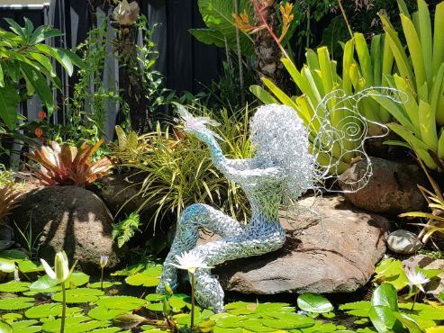 A Statue of a Mermaid is Sitting on a Rock in a Garden Next to a Pond — Omni Builders In Bungalow, QLD