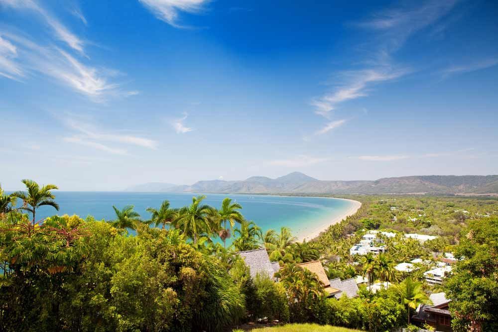 A View Of A Beach From A Hill With Trees And Mountains In The Background — Omni Builders In Port Douglas, QLD