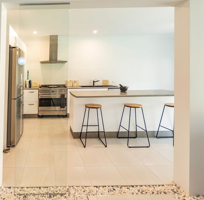 A Kitchen With Stools and a Stove and Refrigerator — Omni Builders In Bungalow, QLD