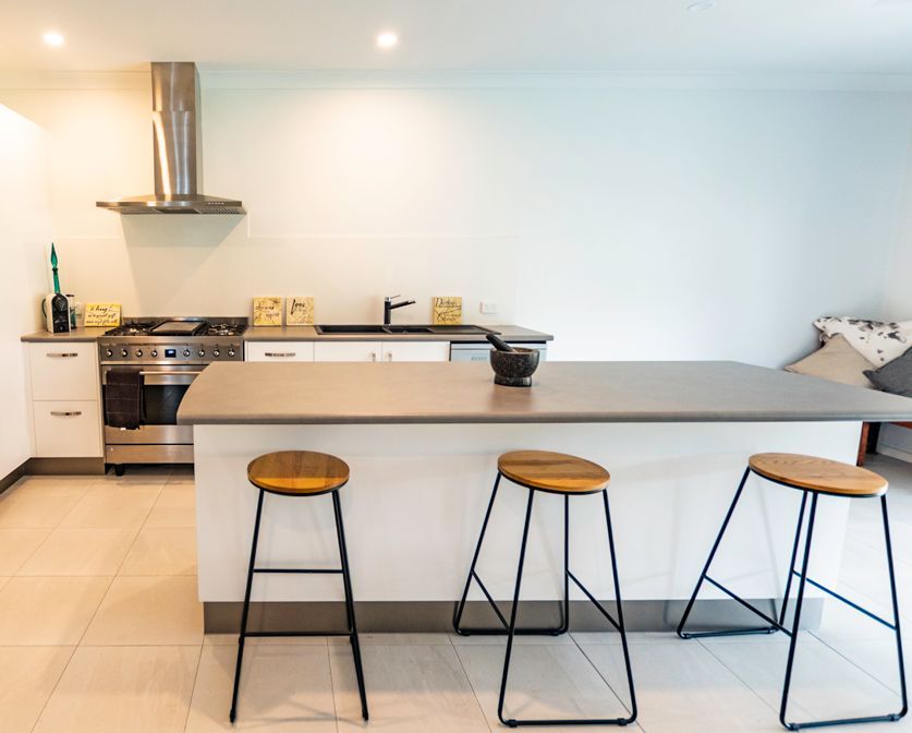 A Kitchen With a Large Island and Three Stools — Omni Builders In Bungalow, QLD