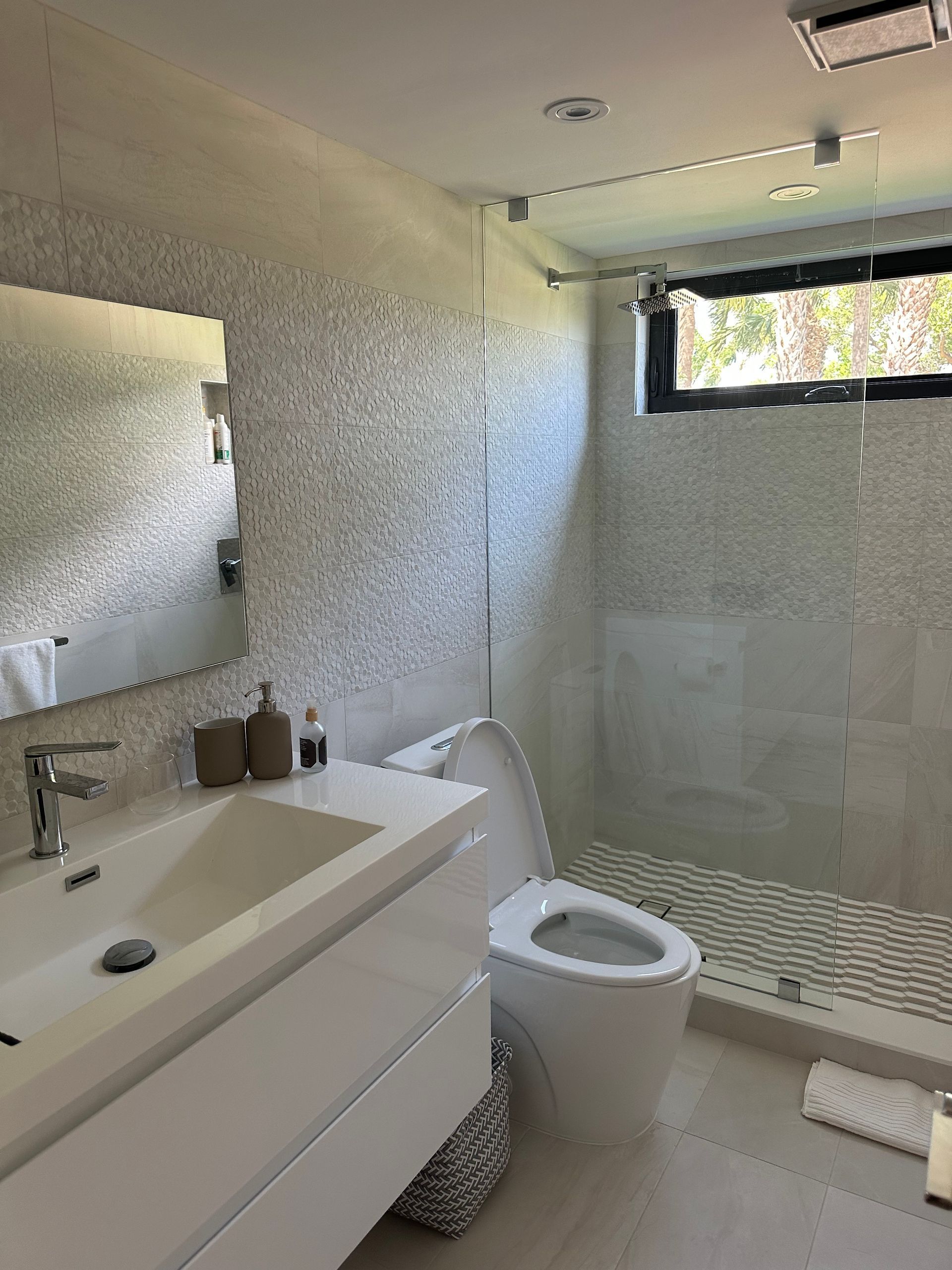A bathroom with a toilet , sink , mirror and walk in shower.