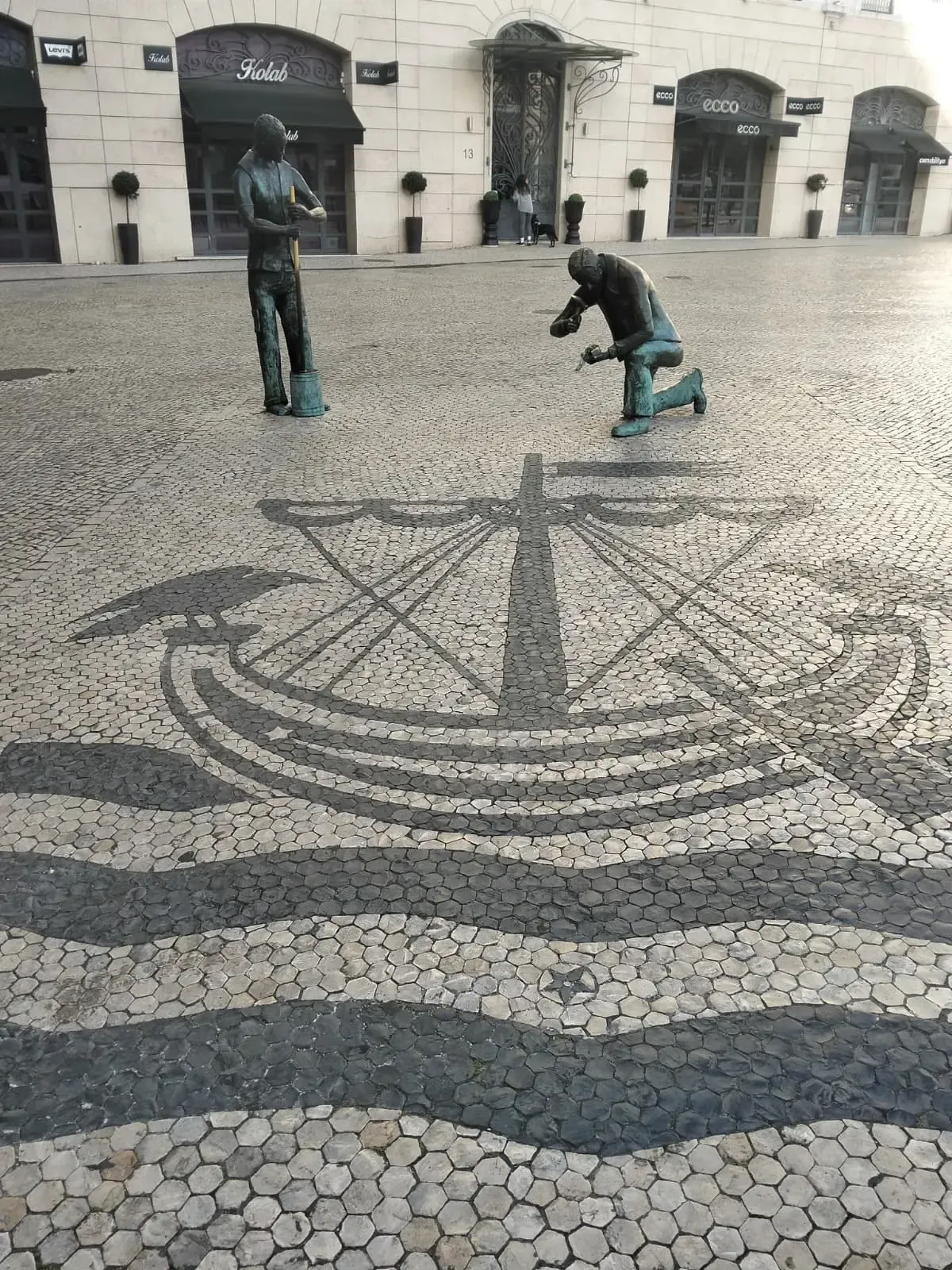 Portuguese cobblestone mosaic of a compass rose with bronze statues in Lisbon downtown