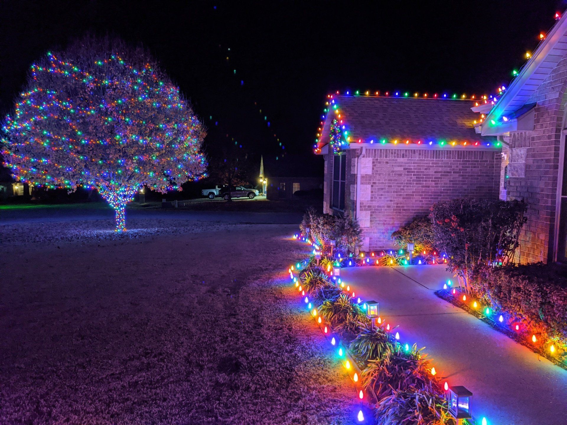 Christmas lights wrapped on a tree and a lit wreath on a home showing off lights hung by top quality home services