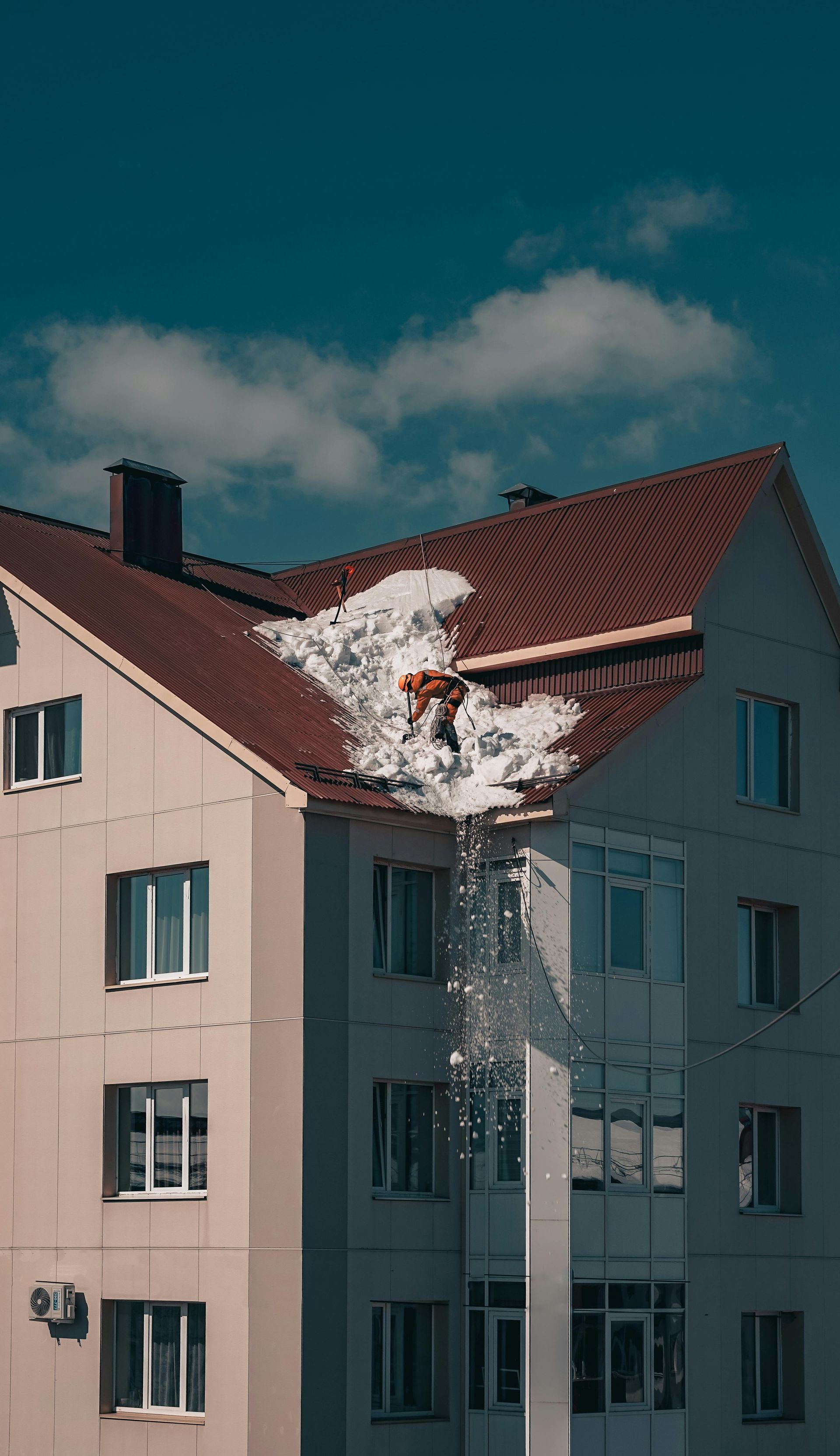 A person is cleaning snow from the roof of a building.