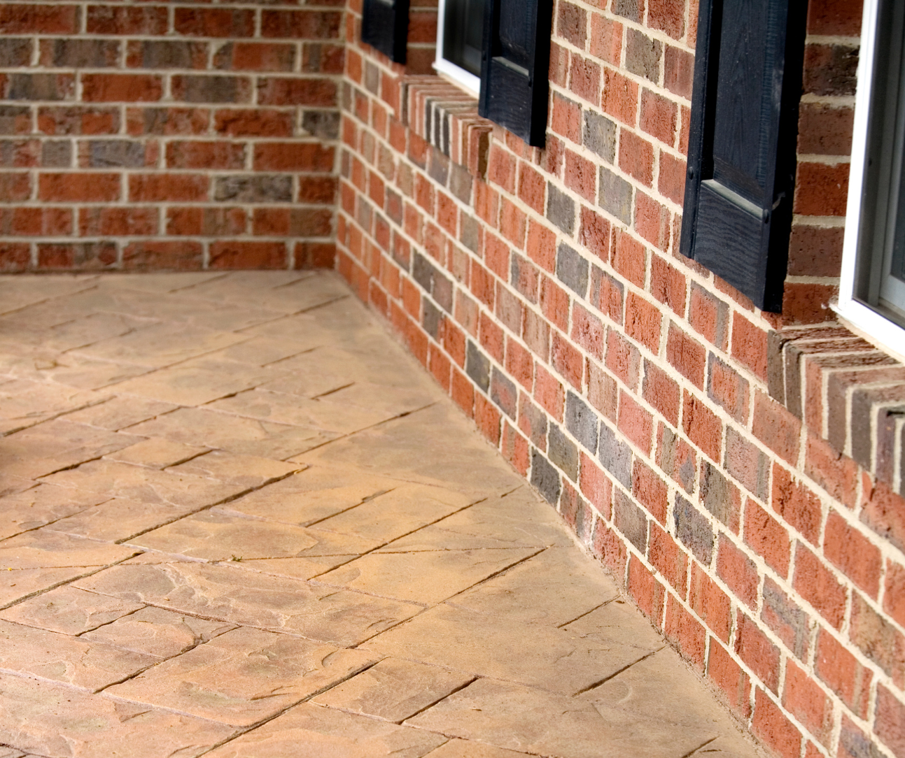 Brick patio beside a red brick house with tan stamped concrete flooring and windows Brick patio beside a red brick house with tan stamped concrete flooring and windows