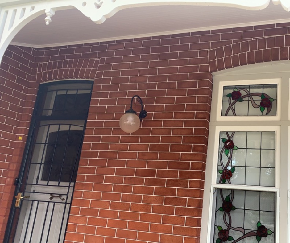 Brick house exterior with black door, wall lantern, and stained-glass window panes Brick house exterior with black door, wall lantern, and stained-glass window panes