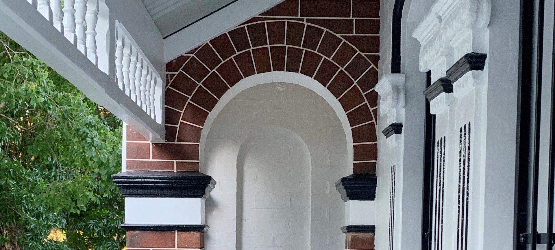 Front porch with a brick archway, white trim, and striped columns beside a doorway