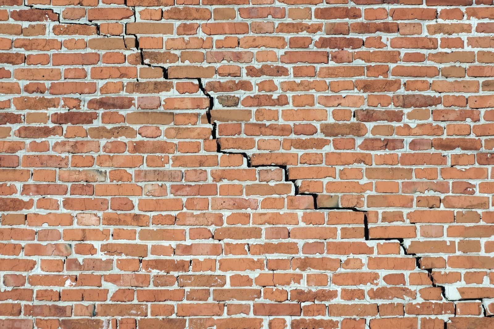 Cracked red brick wall with a jagged diagonal fracture and missing mortar lines
