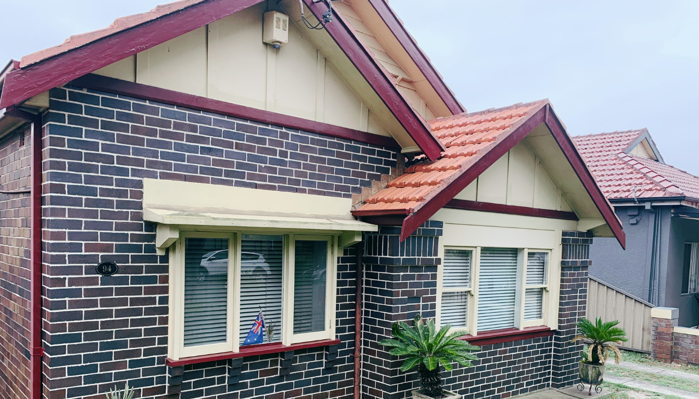 Brick house with cream trim and red roof, showing front windows and a small garden.