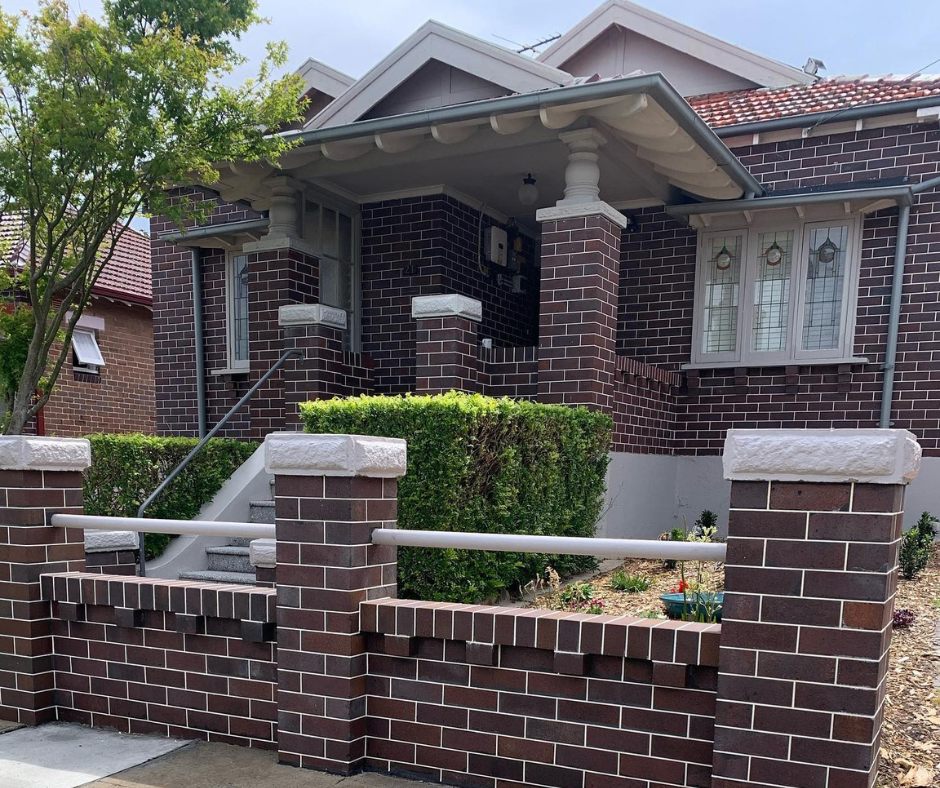 Brick house with a front porch, trimmed hedges, and a low brick fence in front.