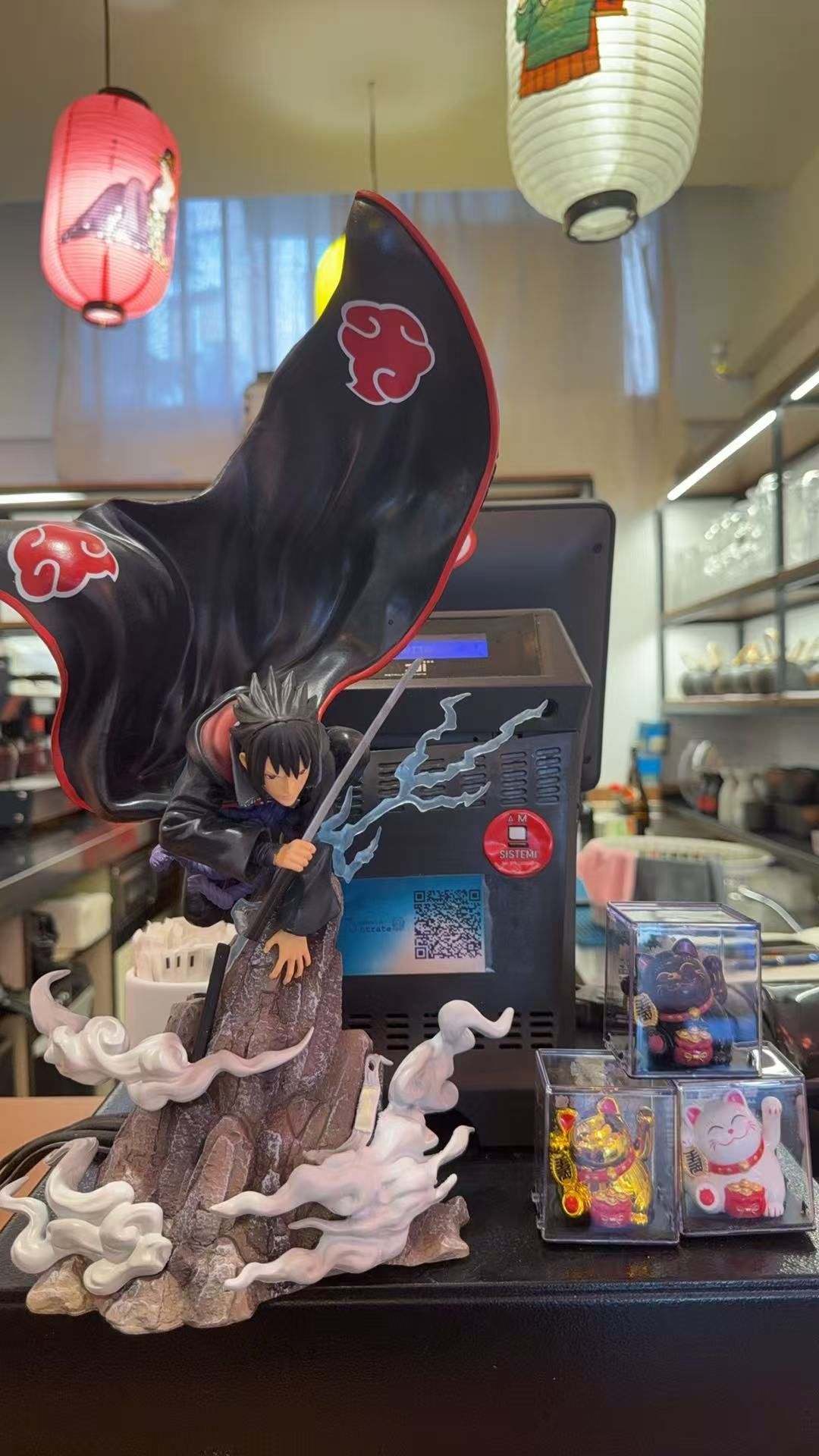 Espositore per action figure anime con una grande figura alata nera, lanterne e scatole da collezione su uno scaffale