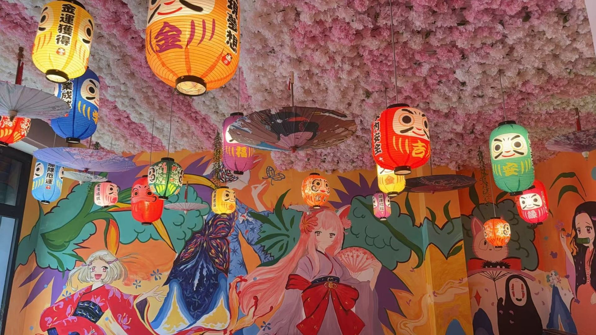 Lanterna colorata appesa sopra un murale dipinto raffigurante persone in una vivace scena di festa al chiuso.