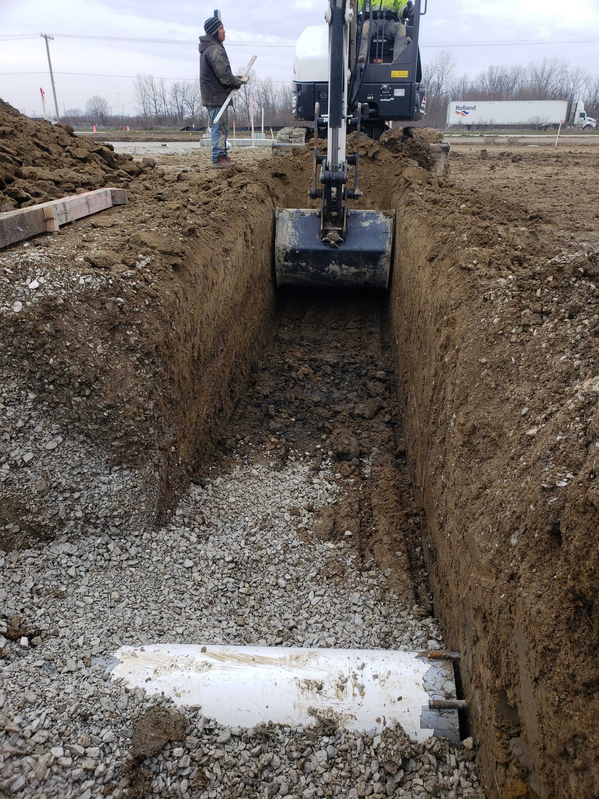 A man is standing in a trench next to a small excavator.