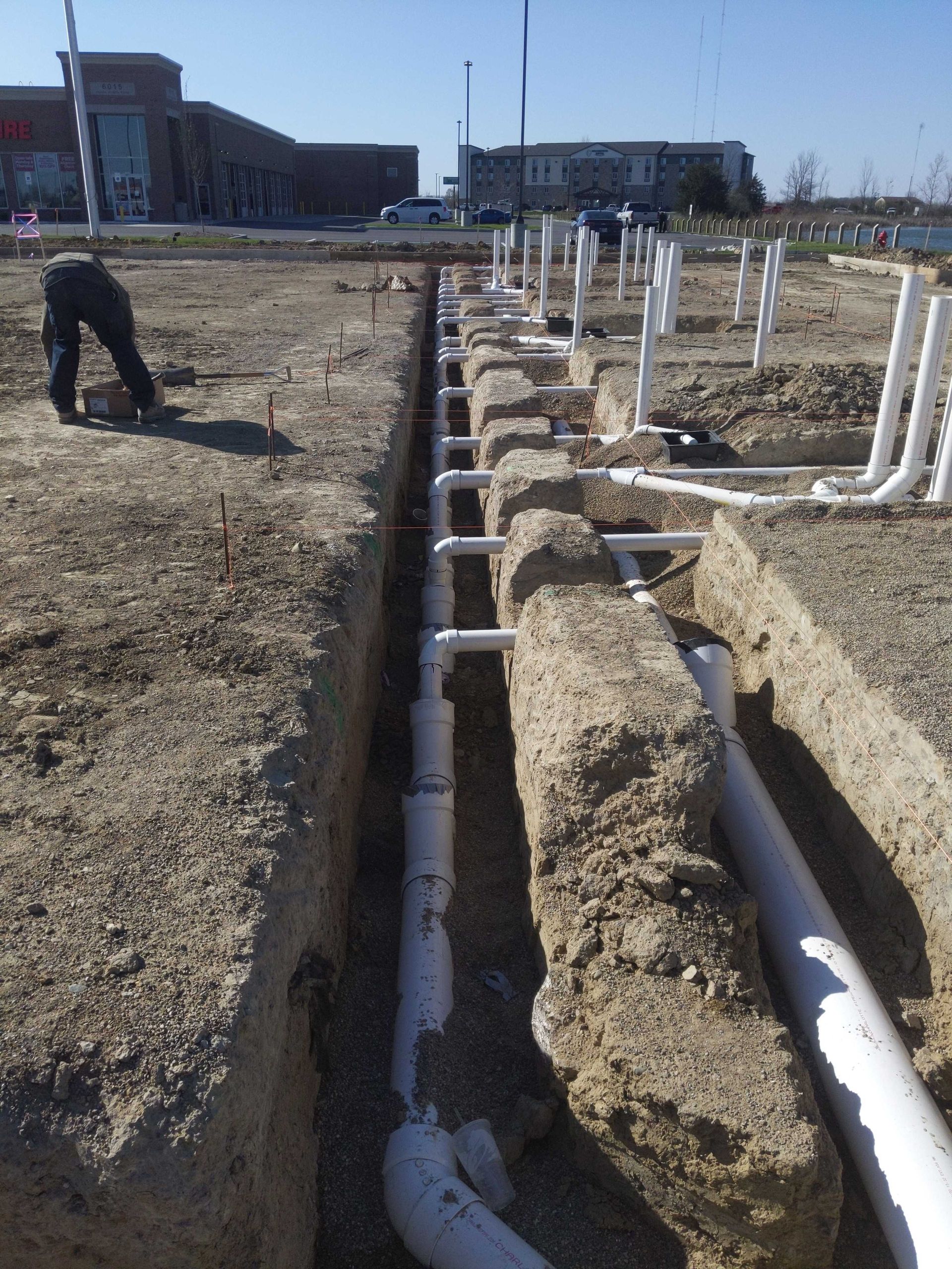 A man is laying pipes in the dirt in front of a building