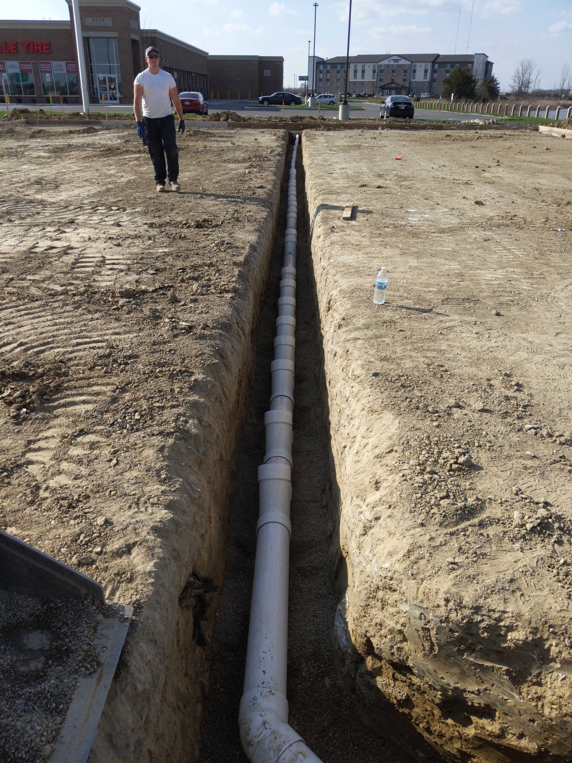 A man is standing in a trench next to a white pipe