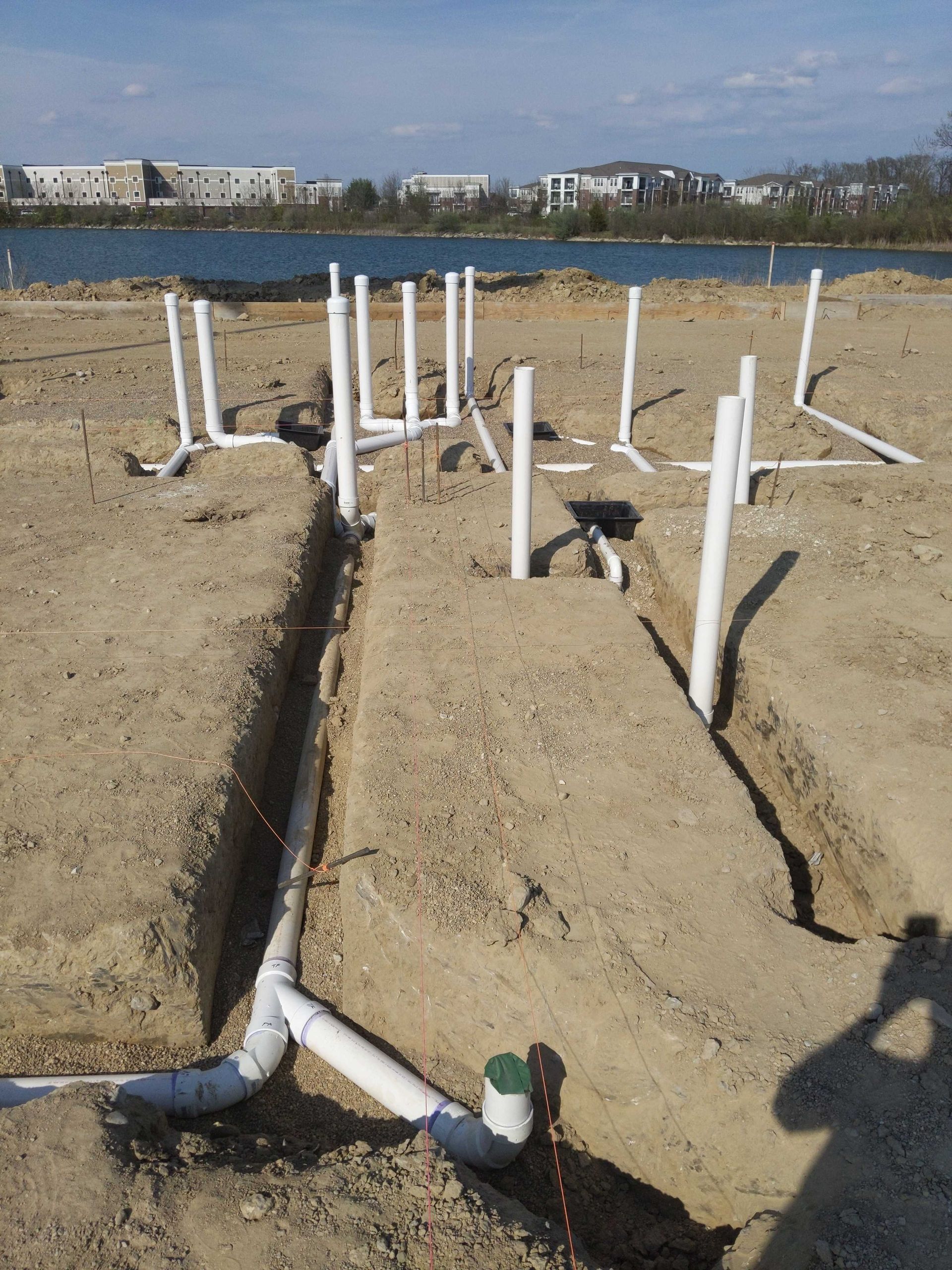 A bunch of white pipes are in the dirt near a body of water
