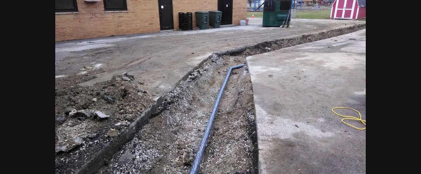 A pipe is being installed in the dirt in front of a building.