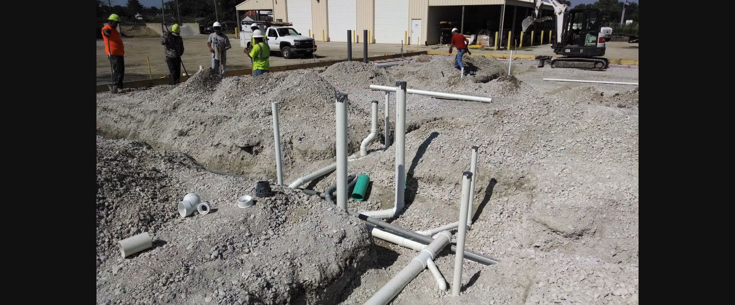 A bunch of pipes are laying in the dirt on a construction site.
