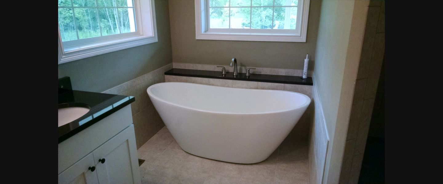 A bathroom with a tub , sink , and window.