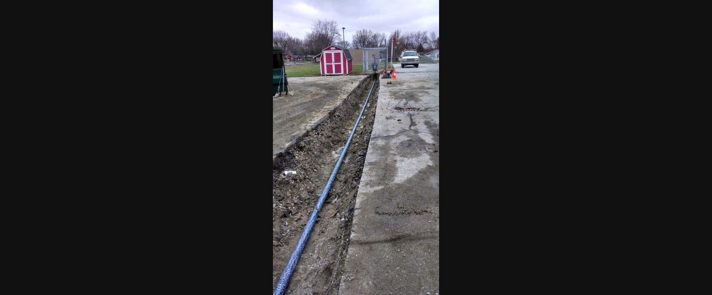 A blue pipe is laying in the dirt next to a sidewalk.