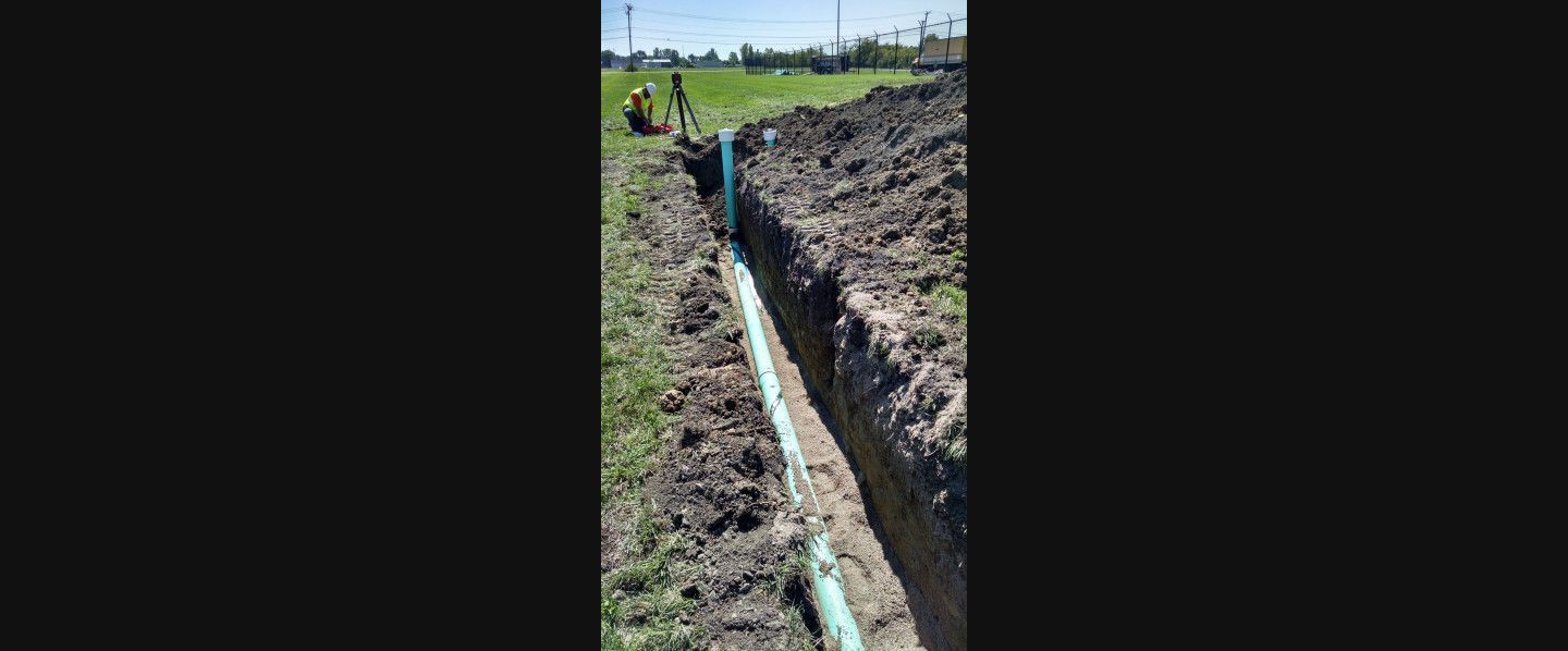 A green pipe is being installed in a trench in a field.