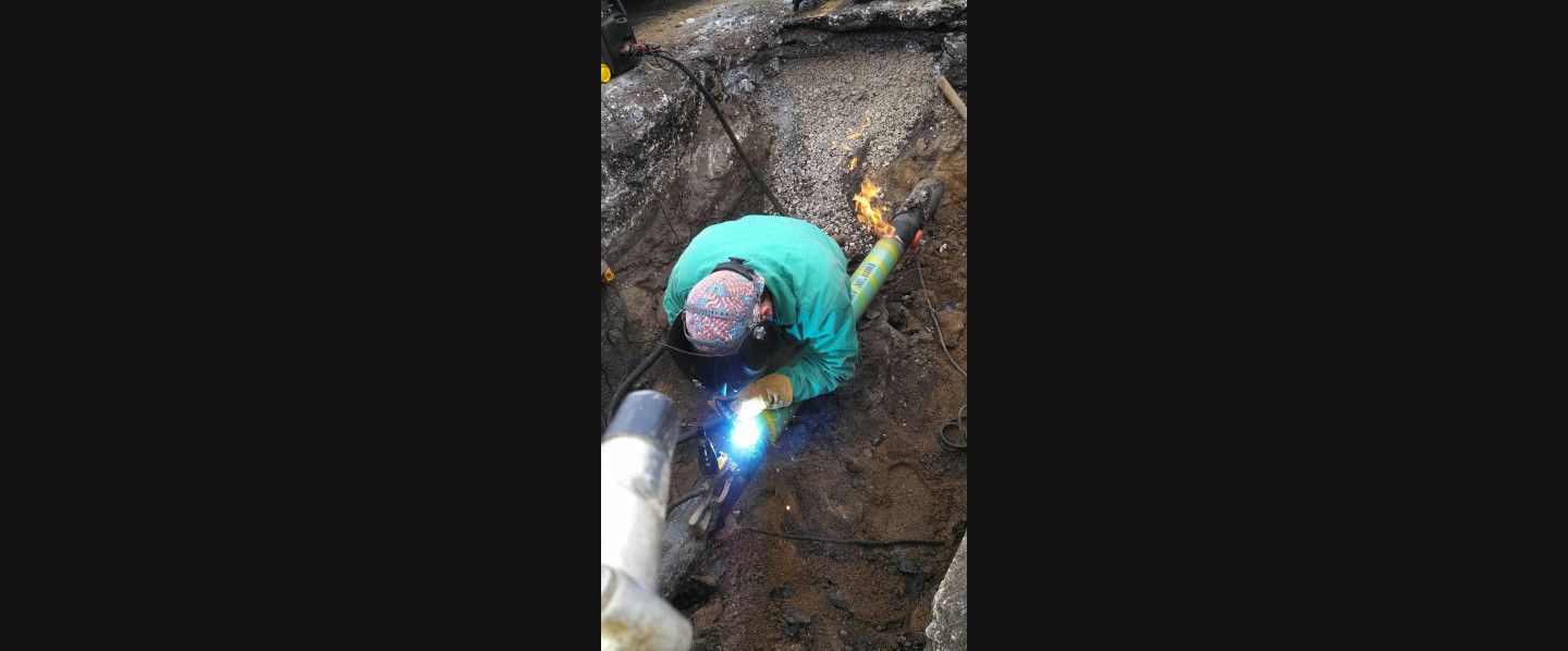 A man is welding a pipe in the dirt.