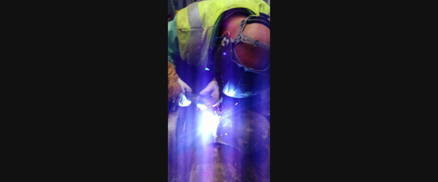 A man is welding a piece of metal in a factory.