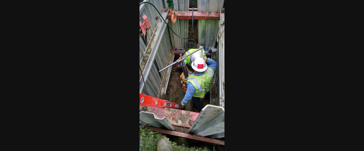 A man in a hard hat is standing in a hole in the ground.