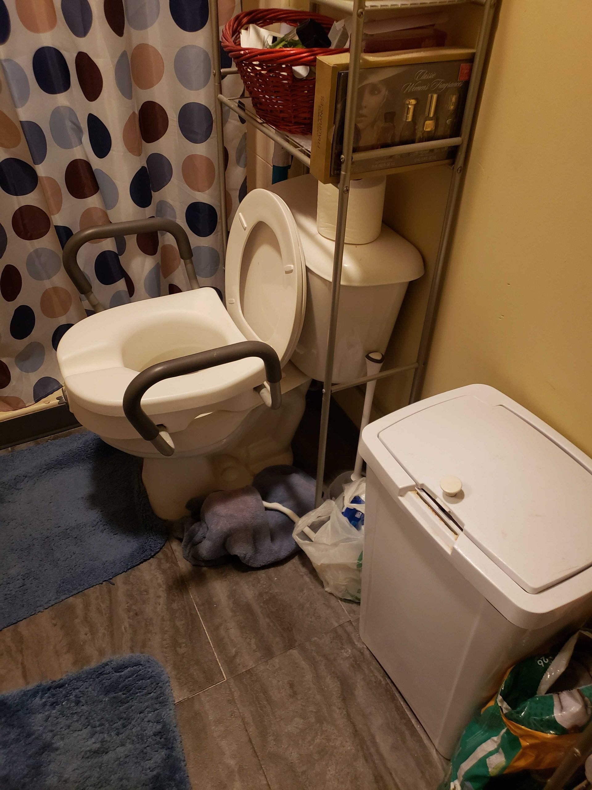 A bathroom with a toilet , trash can , and shower curtain.
