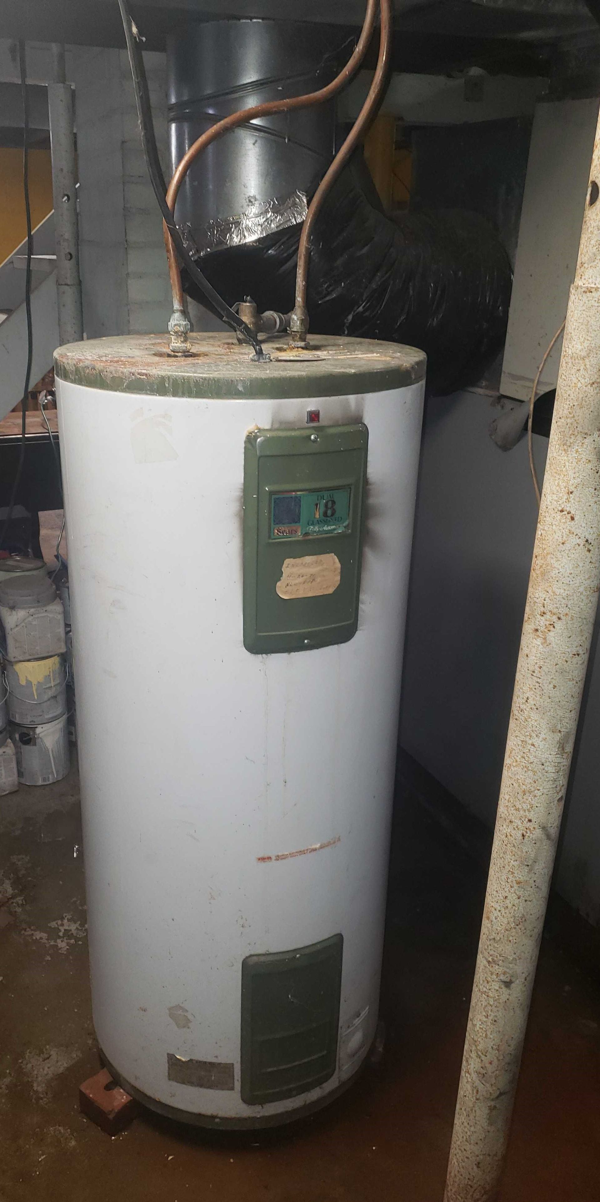 A white water heater is sitting in a basement next to a pipe.