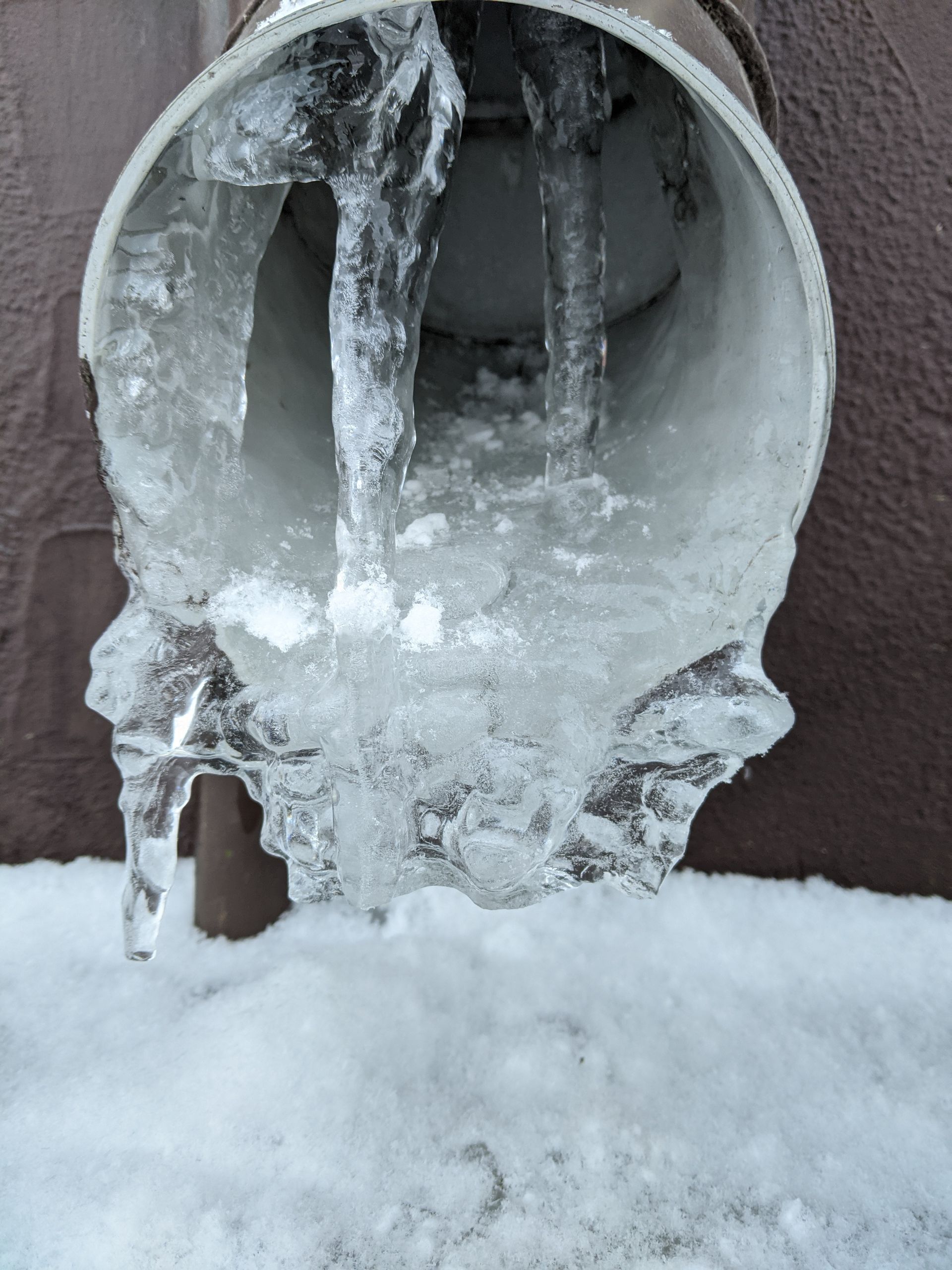 A pipe is covered in ice and water is coming out of it