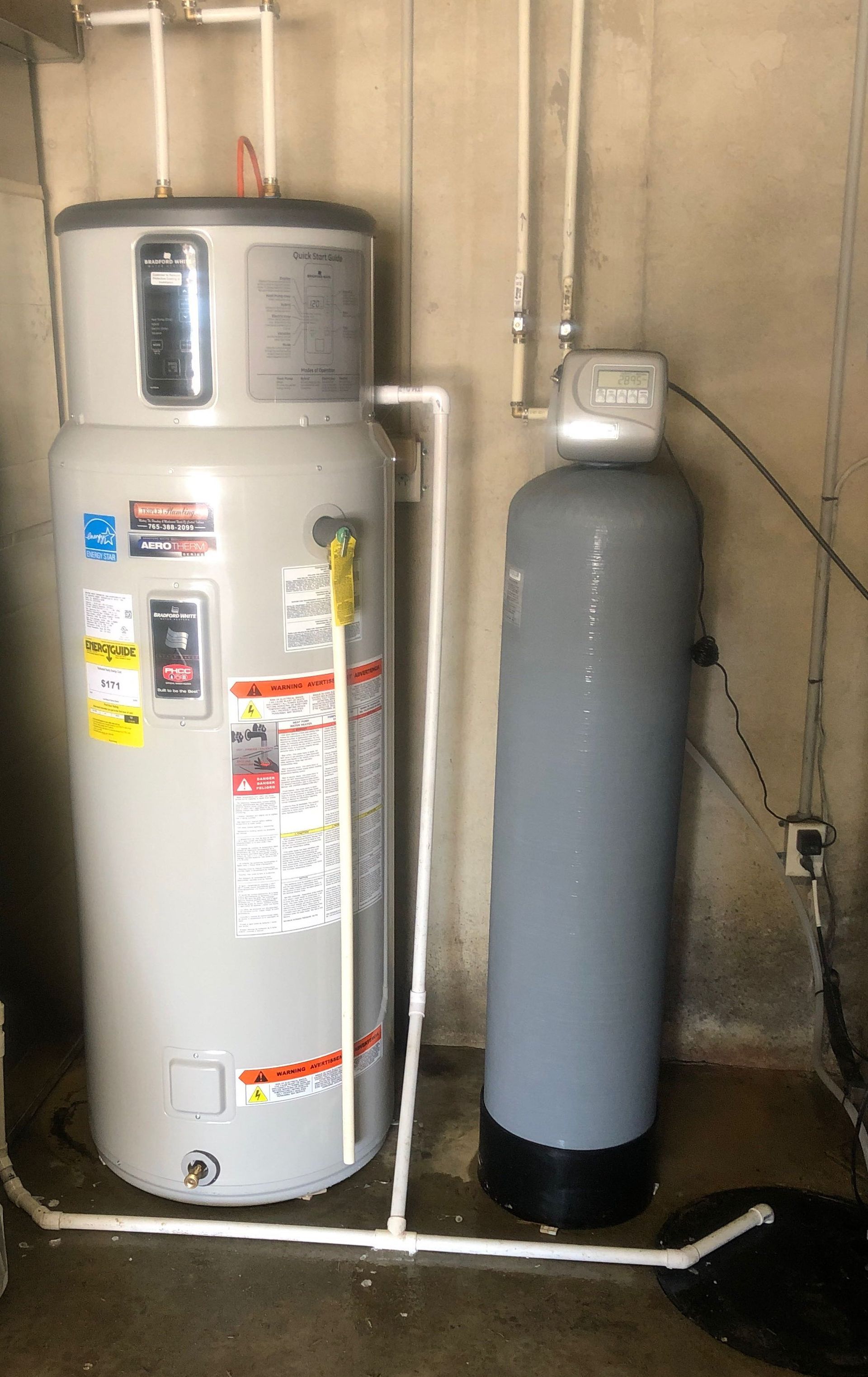 A water heater is sitting next to a water filter in a basement.