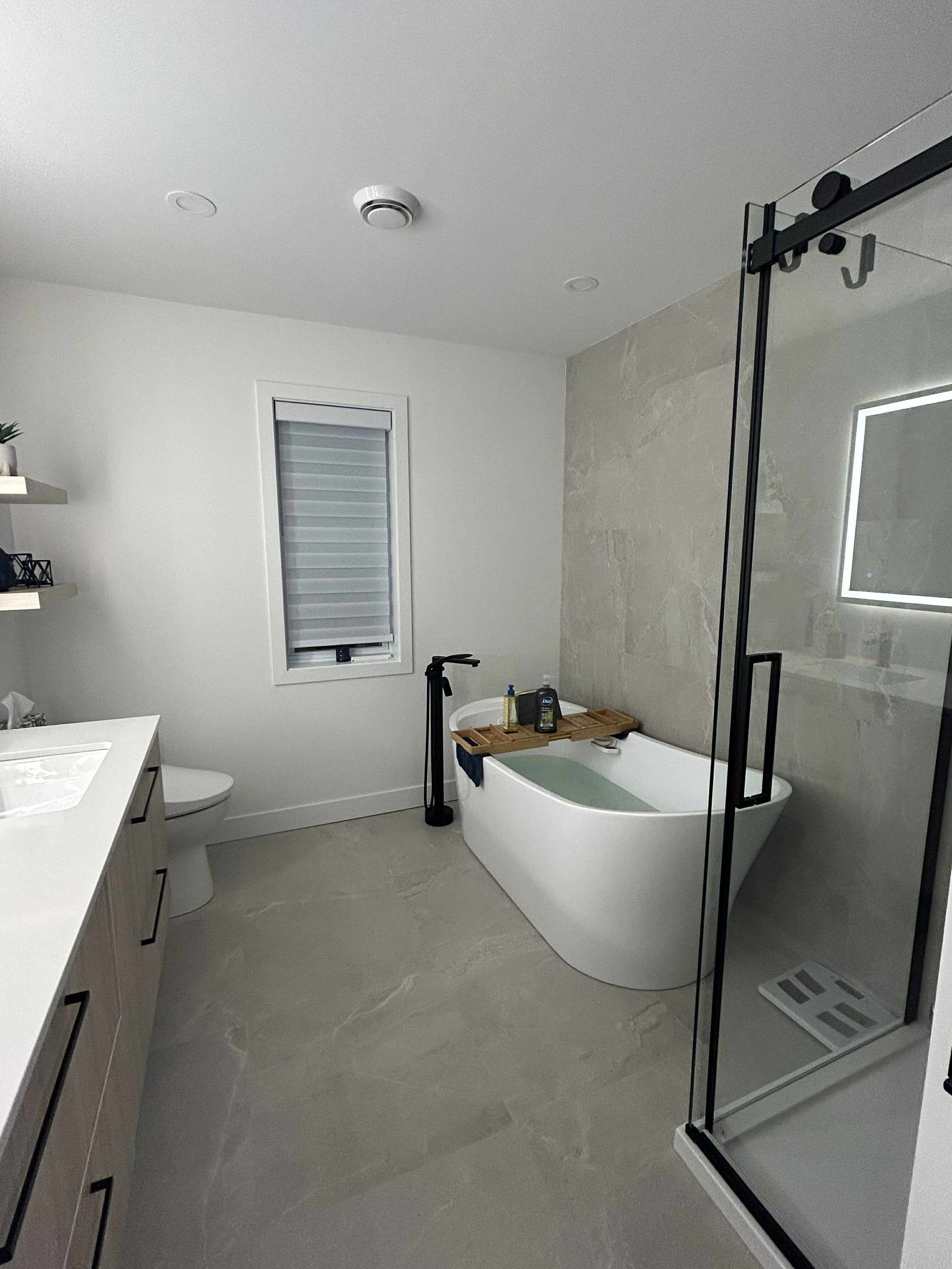 Salle de bains moderne avec un meuble-lavabo clair, une baignoire blanche sur pieds près d'une fenêtre et une cabine de douche en verre.